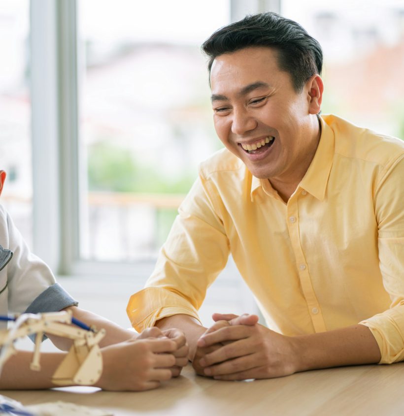 Happy smiling Asian male teacher teaching and telling funny story to group of students